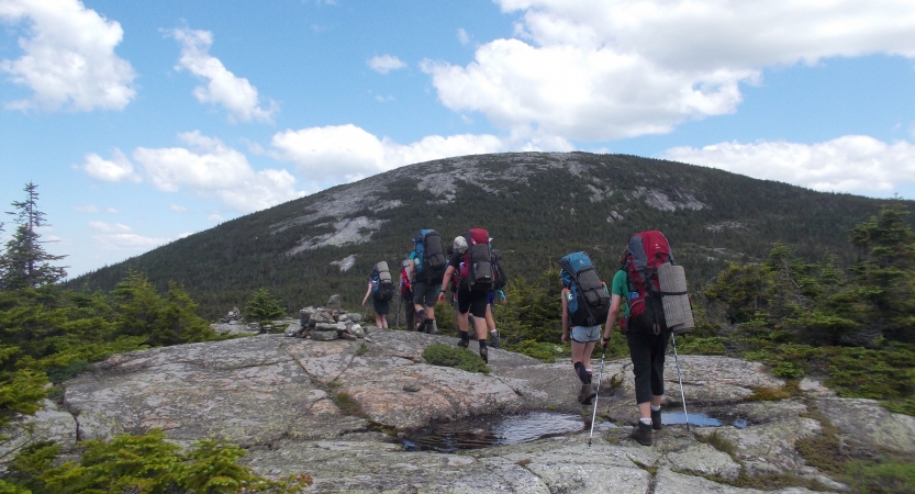 A group of backpackers hike over rocky terrain toward a mountain. 